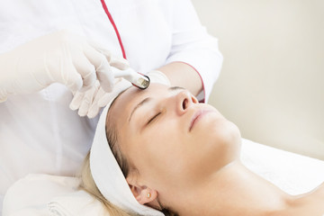 The woman undergoes the procedure of medical micro needle therapy with a modern medical instrument derma roller. 