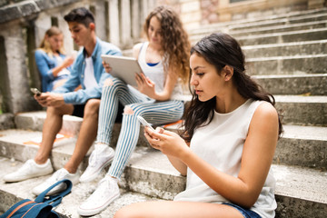 Teenagers with smartphones and tablets on stone steps.