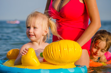 Close-up a little girl swims in the sea with her sister and mother.