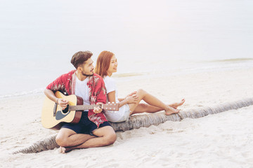 Happy young asian couple playing guitar at the beach
