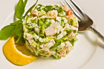 chopped shrimp salad on a white, round plate with a slice of lemon and a sprig of basel and an artisan fork, paleo diet