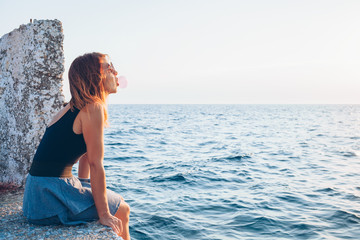 Young woman sitting on the pier enjoying the view of the sea