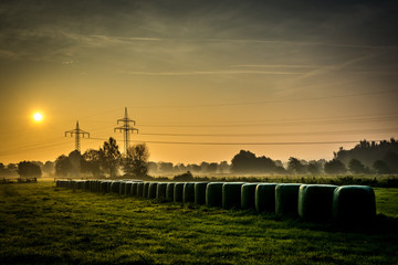 Fototapeta na wymiar Sunrise in foggy fields with hay bales