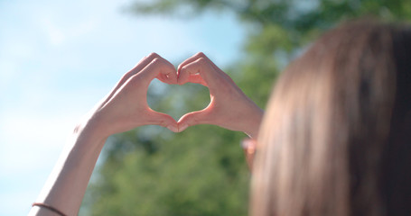 Female hands in shape of heart over green nature and blue sky. 