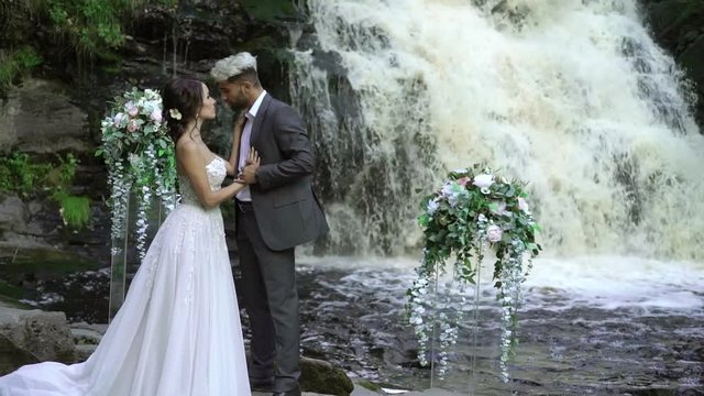 Young wedding couple staying at ceremony near waterfall