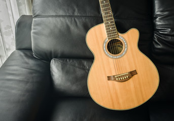Fototapeta premium Acoustic guitar laid on black leather sofa by the living room window.