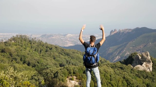 Esploratore con zaino blu saluta soddisfatto dalla cima della montagna scalata