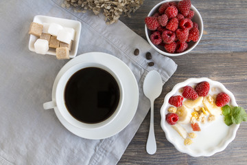 Obraz na płótnie Canvas Healthy breakfast - cup of black coffee, bowl of raspberries, bowl of yogurt or milk with fruits, berries and granola or gorp. Top view.