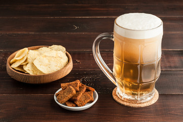 glass of cold frothy lager beer and potato chips plate on wooden table