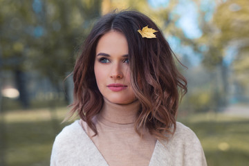 Perfect Woman with Yellow Autumn Leaf in Brown Hair Outdoors. Beautiful Model in Autumn Park