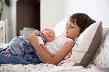 Beautiful boy, hugging with tenderness and care his newborn baby brother at home