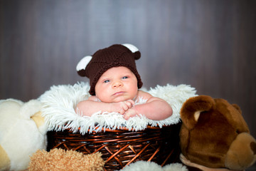 Cute newborn baby boy in basket with teddy bear hat, looking at camera