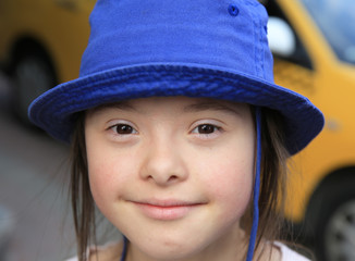 Cute smiling down syndrome girl on the background of taxi