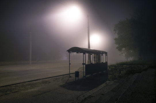Foggy street lights misty with night deserted road and trees with bus stop
