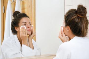 Woman is washing her face with lotion and cotton pads