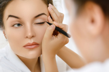 Woman is applying eyeliner - obrazy, fototapety, plakaty