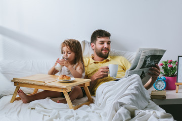 Father and daughter having breakfast in bed