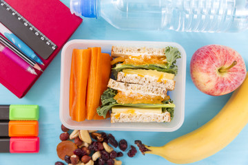 School lunch box with sandwich, vegetables, water, nuts and fruits on turquoise background. Healthy eating habits concept