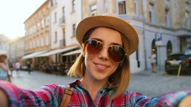 Portrait of young attractive woman in sun glasses with hat posing on the camera in the city street. Close up tourist
