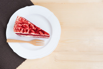 Red Velvet Cake sliced in piece on white plate with wooden spoon over brown placemat & wood table background for celebrate X'mas season, Valentines day or special events, copy space for text insertion