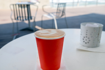 Red disposable cup of coffee standing on a white table on blue sea and beach background