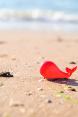 Fototapeta na wymiar Plastic toy red whale on the seashore for background
