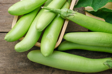 Fresh green eggplant with leaves on wooden table background.
