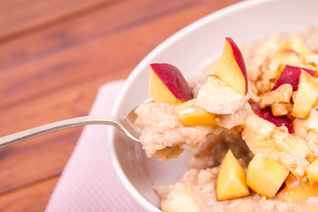 Porridge with peach, apple, banana and walnut on a wooden table
