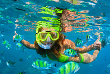 Happy family - girl in snorkeling mask dive with tropical fishes in coral reef sea pool. Travel...