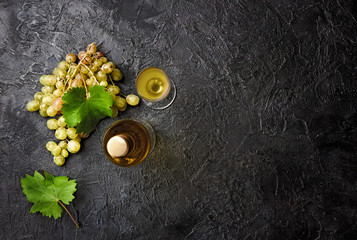 Bottle of white wine with grapes and leaves of grapes on dark concrete background.