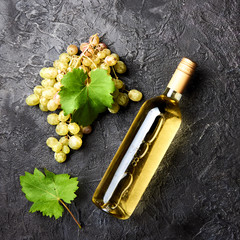 Bottle of white wine with grapes and leaves of grapes on dark concrete background.