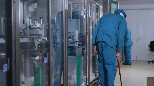Factory worker sweep the floor. Factory operator man sweeping floor near manufacturing equipment. Factory interior cleaning service. Man brooming in factory workshop