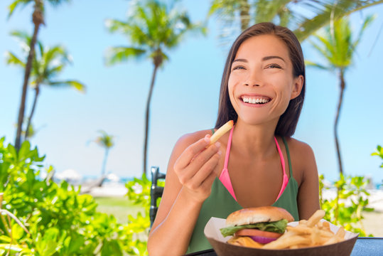 Woman Eating French Fries Food At Resort Restaurant. Asian Girl Enjoying Summer Vacation At Beach Bar With Fast Food Lunch Meal, Burger And Fries.