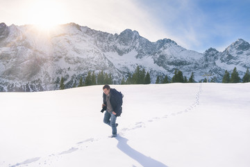Fototapeta na wymiar Man walking through snow in mountains - Representative image of the winter season, with snowy mountain peaks, fir forest and a man wandering through a thick layer of snow, in Ehrwald, Austria.