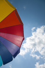 Colorful beach umbrella against blue sky with clouds. Vertical.