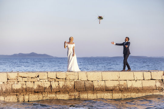 Bride and groom on pier throwing bouquet into air
