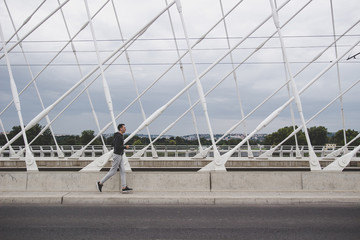 Naklejka premium Young man running on the modern bridge in the city, listening music on smartphone