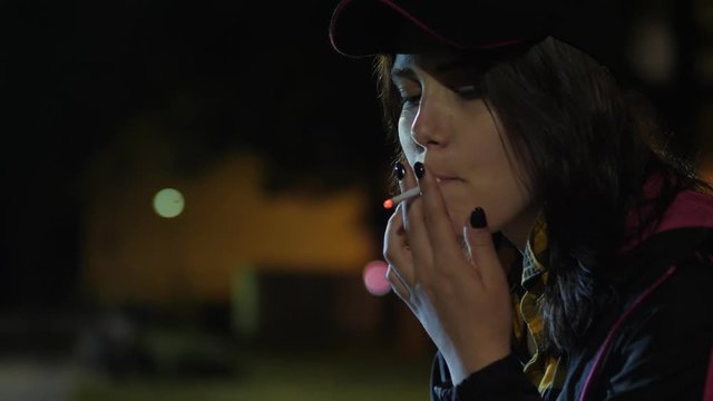 An angry sad teen girl with a cigarette. Night in park.