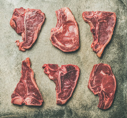 Flat-lay of fresh raw beef meat steak cuts over grey concrete background, top view. Porterhouse, t-bone and rib-eye steaks. Butcher' s shop or cooking meat dinner concept