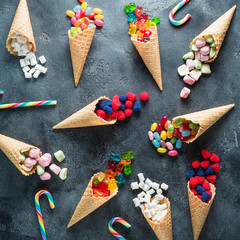 Colorful bright assorted candy in waffle cones on dark background. Flat lay, top view