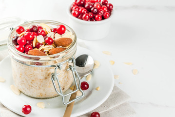 Recipe for a healthy winter breakfast, ideas for Christmas morning. Overnight oatmeal with almonds, cranberries, sugar. On a white marble table. copy space
