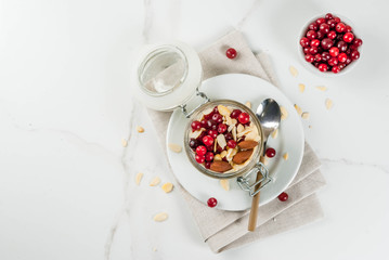 Obraz na płótnie Canvas Recipe for a healthy winter breakfast, ideas for Christmas morning. Overnight oatmeal with almonds, cranberries, sugar. On a white marble table. copy space top view