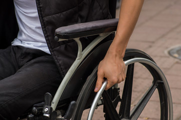 Fototapeta na wymiar Close-up of male hand on wheel of wheelchair during walk in park