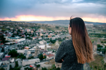 Young woman tourist from a high point looking at the sunset over the city of Goreme in Cappadocia...