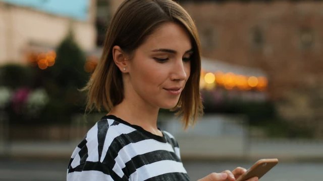 Side View Of Handsome Woman In Denim Shirt Walking Through The City Using Online Maps In Smartphone In The City Street. Close Up.