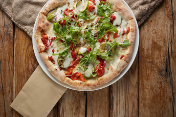 Rounded homemade pizza with paprika, basil, cheese at wooden background.
