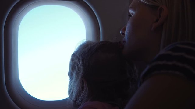 Close up view of cute young girl with her mom looking in illuminator of airplane during the flight.