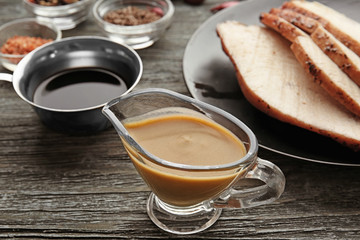 Glass sauce boat with tasty turkey gravy and meat on table