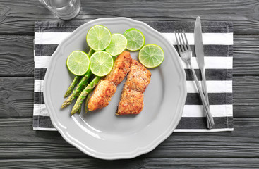 Plate with delicious salmon, sliced lime and asparagus on wooden table