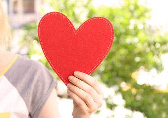 Fototapeta na wymiar Woman holding red heart on blurred background. Volunteer concept